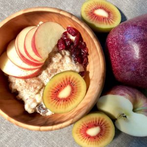 Houten kom met havermout, kaneel, stukjes appel, rode kiwi en granaatappel.