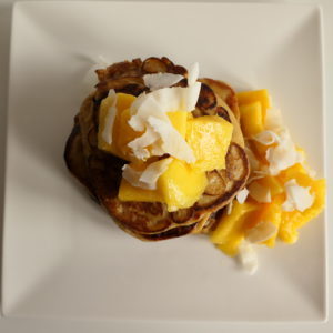 Protein pancakes met stukken mango en kokossnippers op wit bord